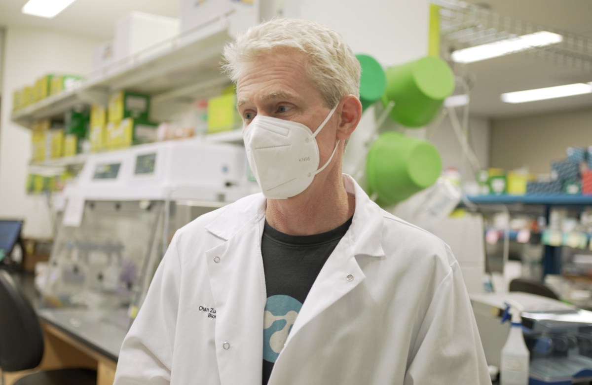 Joe DeRisi in white lab coat wears a N-95 mask in a COVID-19 lab.