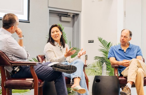 Priscilla Chan speaks while gesturing during a panel discussion, with Steve Quake listening beside her and another panelist engaged.