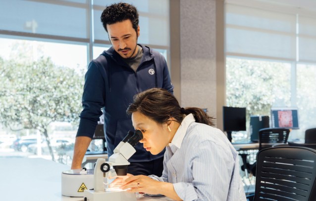 Priscilla Chan looks into a microscope while a colleague observes her in a well-lit laboratory at the CZ Imaging Institute.