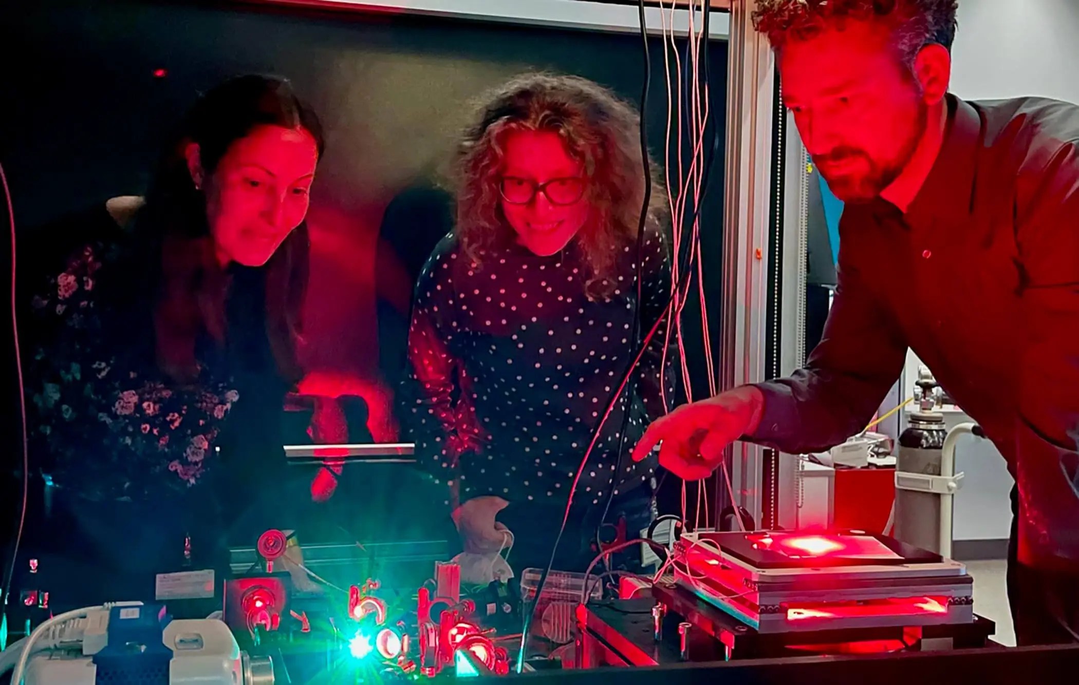 Three people work in a lab and marvel at a green light.