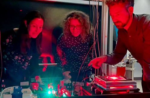 Three people work in a lab and marvel at a green light.