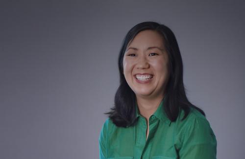 A woman smiles wearing a green shirt against a grey background.